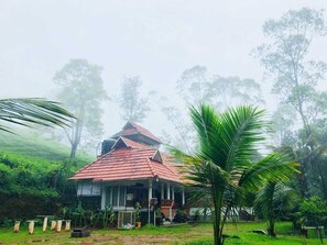 A traditional house with a red tiled roof, surrounded by lush greenery and palm trees. - Snow Valley Munnar (Anachal)