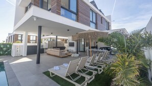 A modern two-story house with a covered patio, outdoor seating, and a swimming pool. - Protaras Aqua Pearl Villa Aq18 (Paralimni)