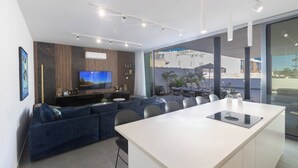A modern living room with a large TV, a sofa, and a dining area with a long table. - Protaras Aqua Pearl Villa Aq18 (Paralimni)