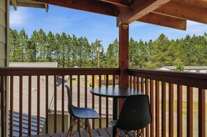 A wooden deck with a table and two chairs, overlooking a forested area.