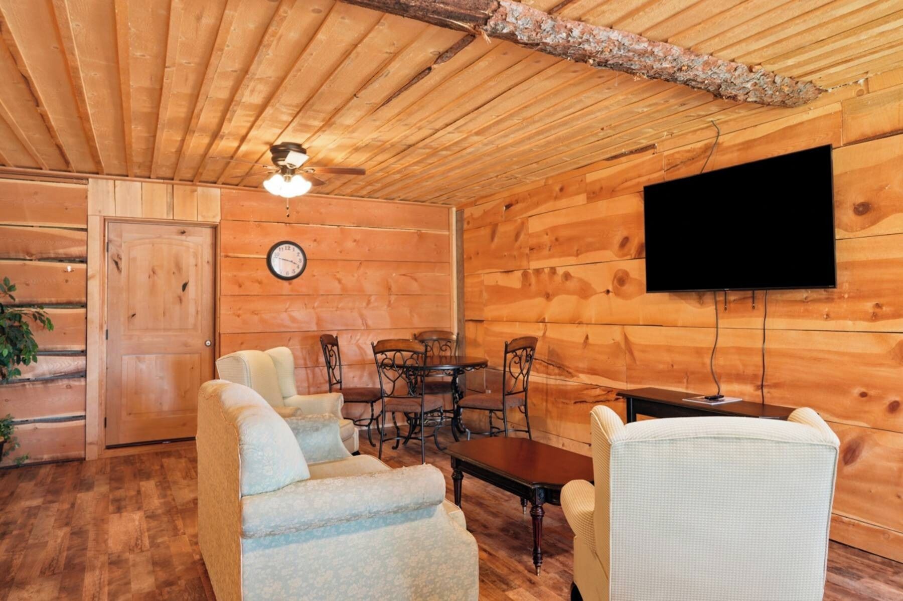 Un intérieur en bois comprenant un coin repas, un canapé, un téléviseur fixé au mur et une horloge.