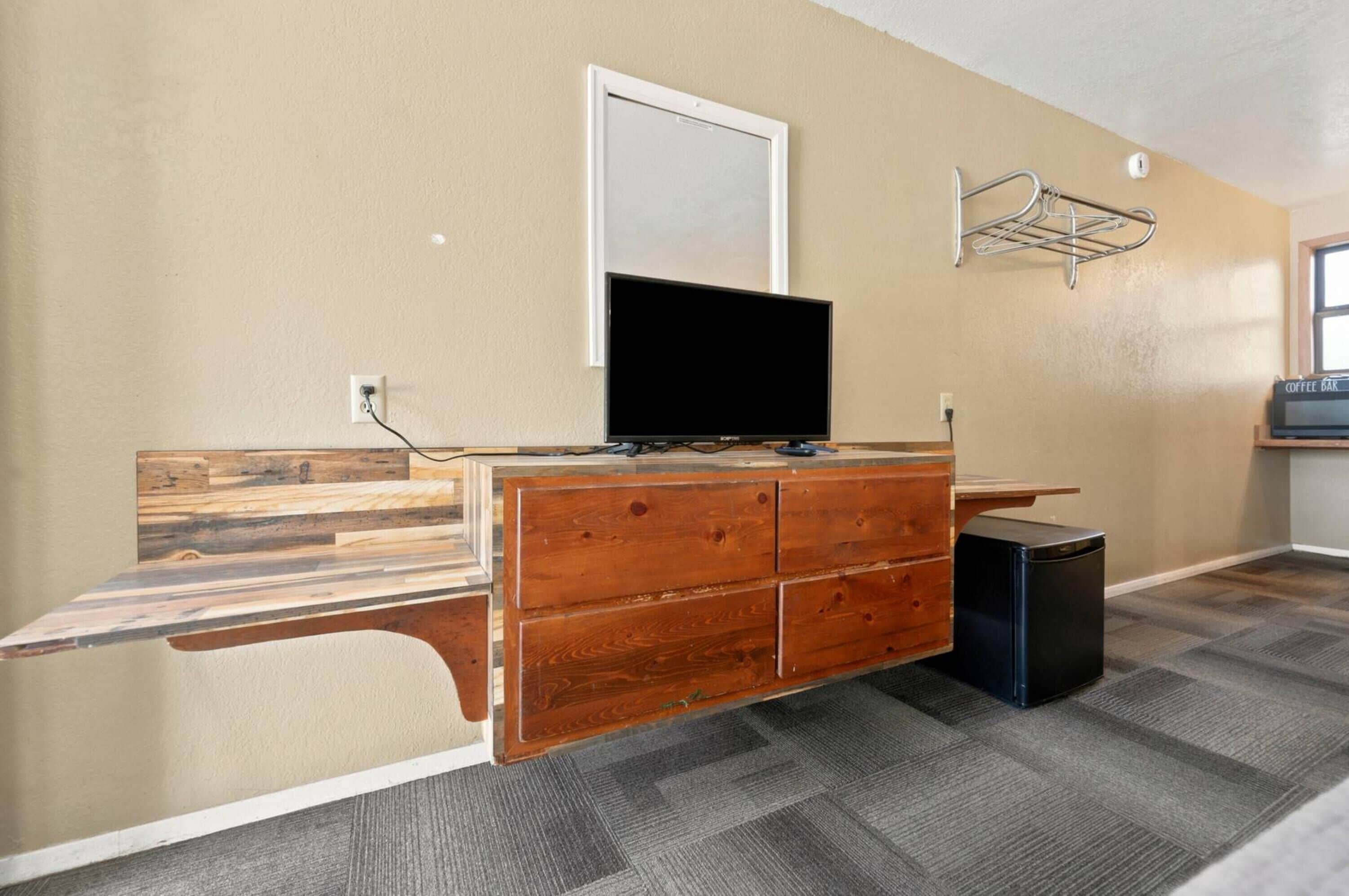 A room with a wooden desk, a television, a small black speaker, and a coffee bar sign on the wall.