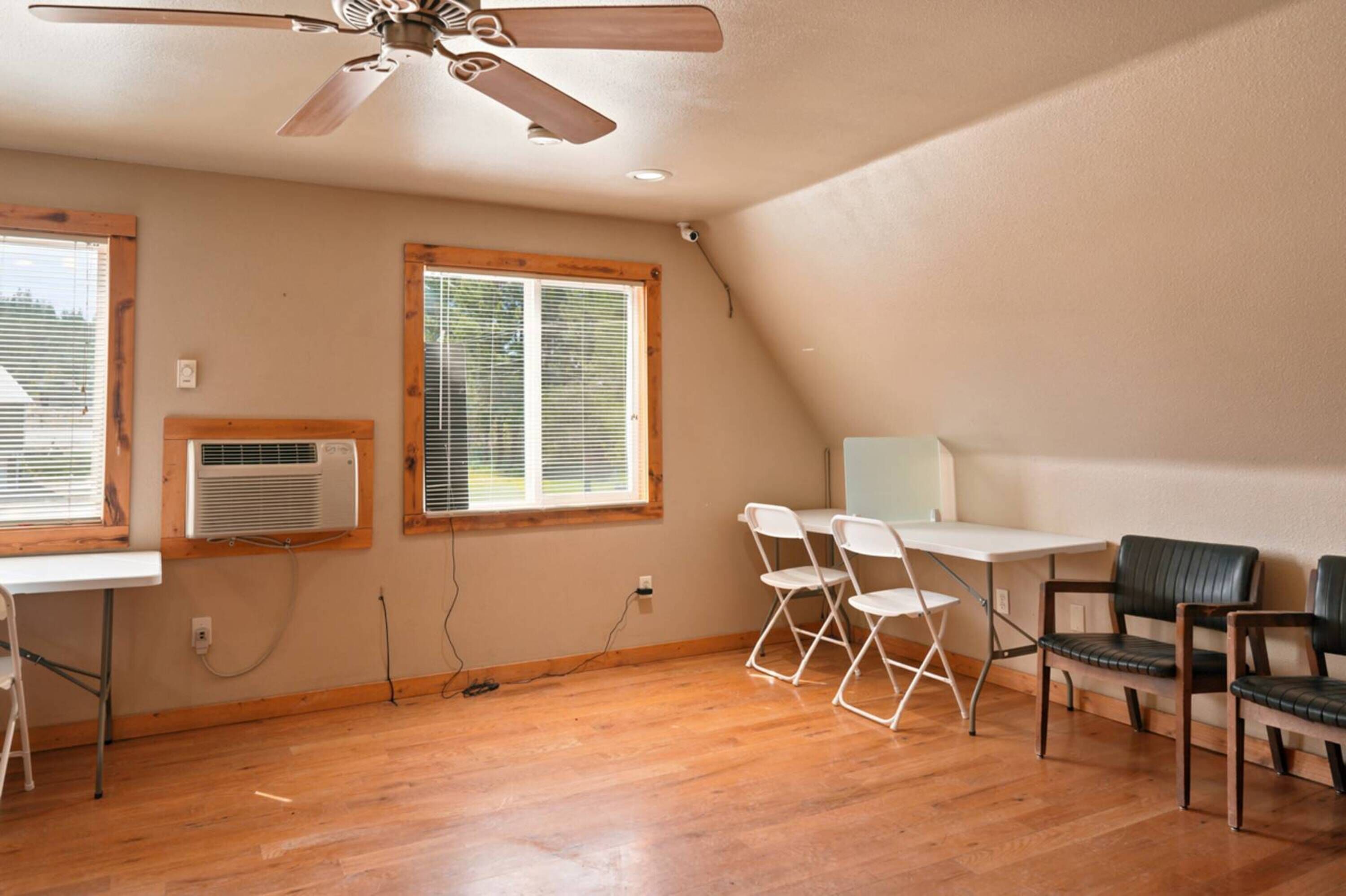 A room with a ceiling fan, two windows with blinds, a white table, and four chairs.