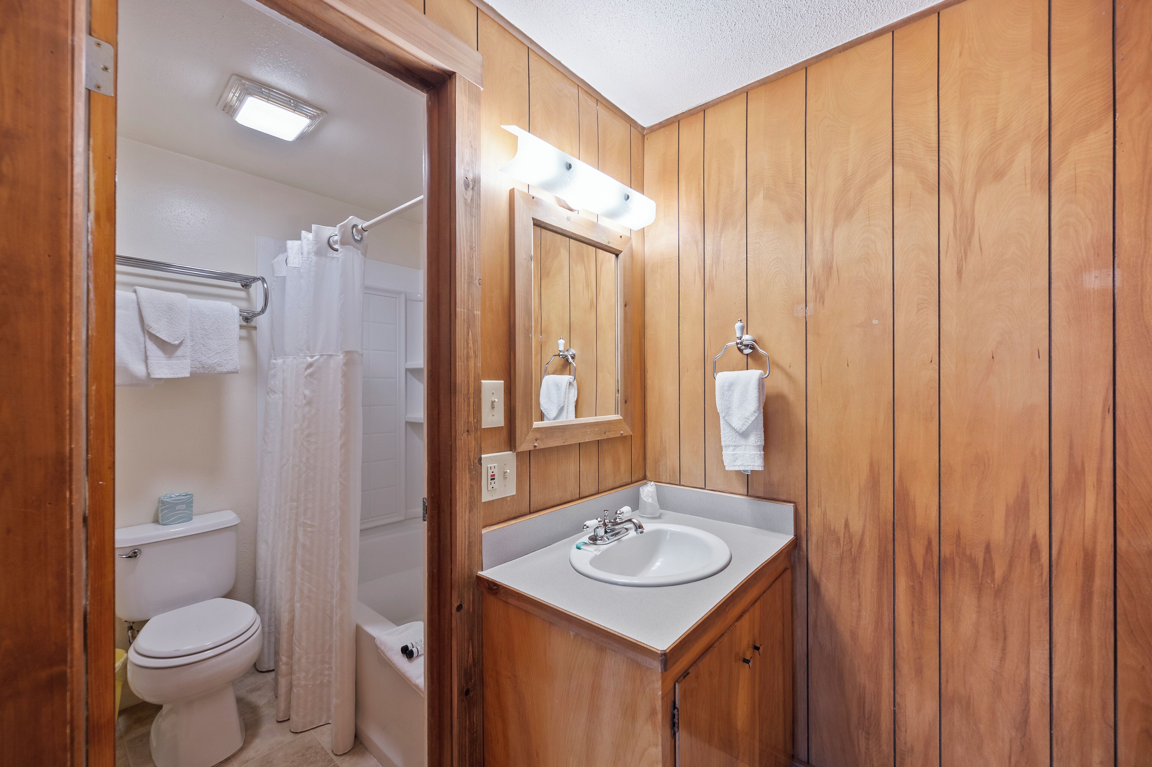 Un baño con paneles de madera, un lavamanos blanco, un espejo y una cortina de ducha.