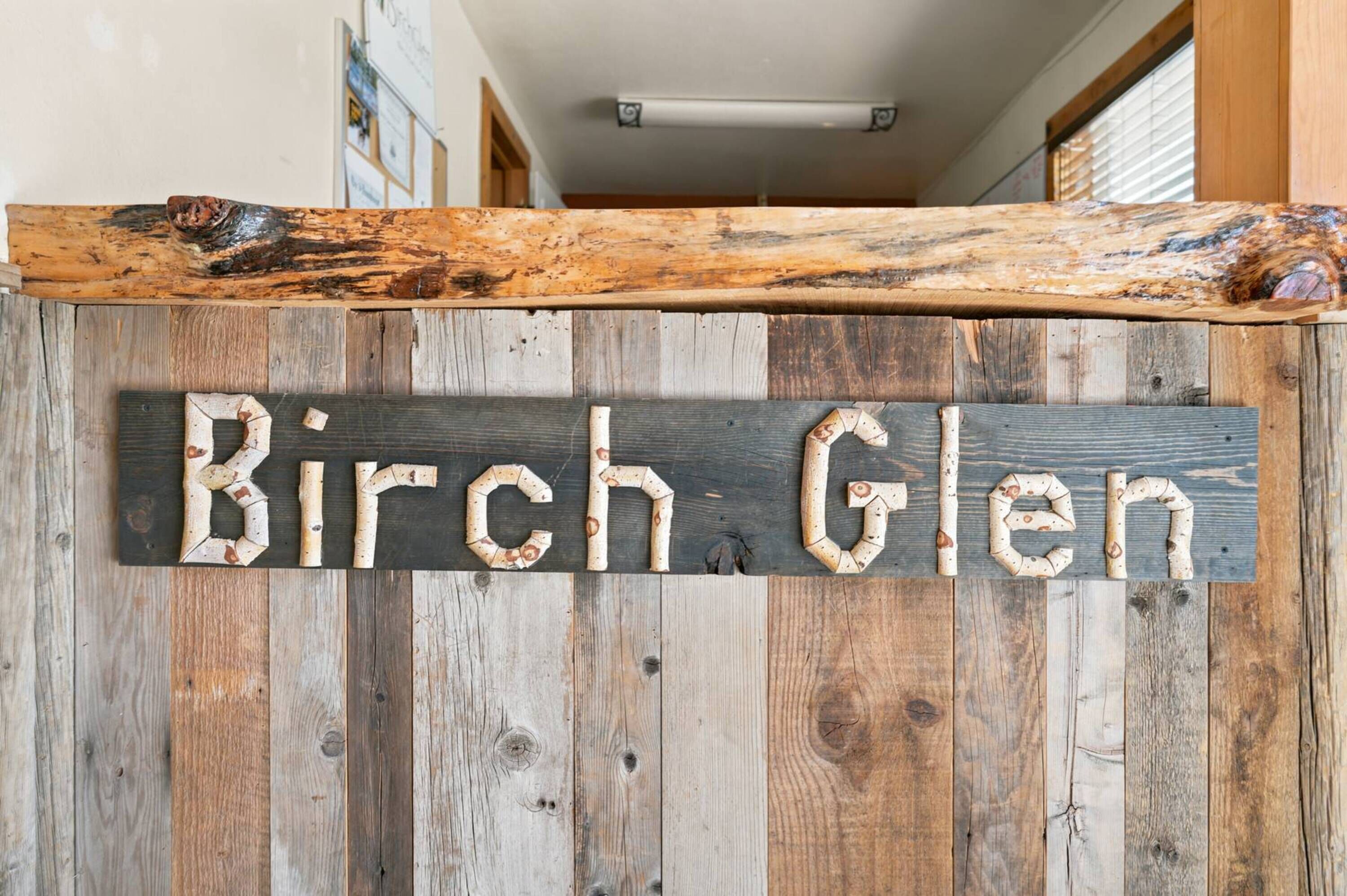 A rustic wooden sign with the text 'Birch Glen' against a backdrop of vertical wooden planks.