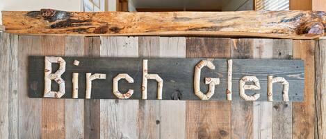 A rustic wooden sign with the text 'Birch Glen' against a backdrop of vertical wooden planks.