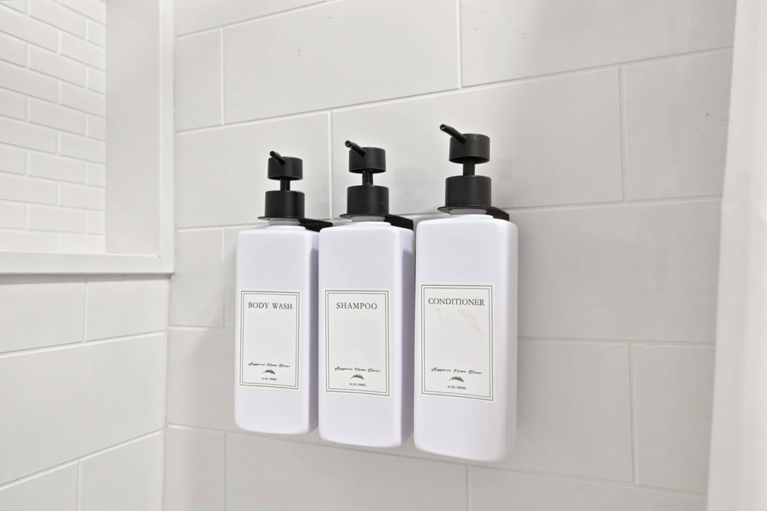 Three white bottles with black pumps on a white tiled wall.