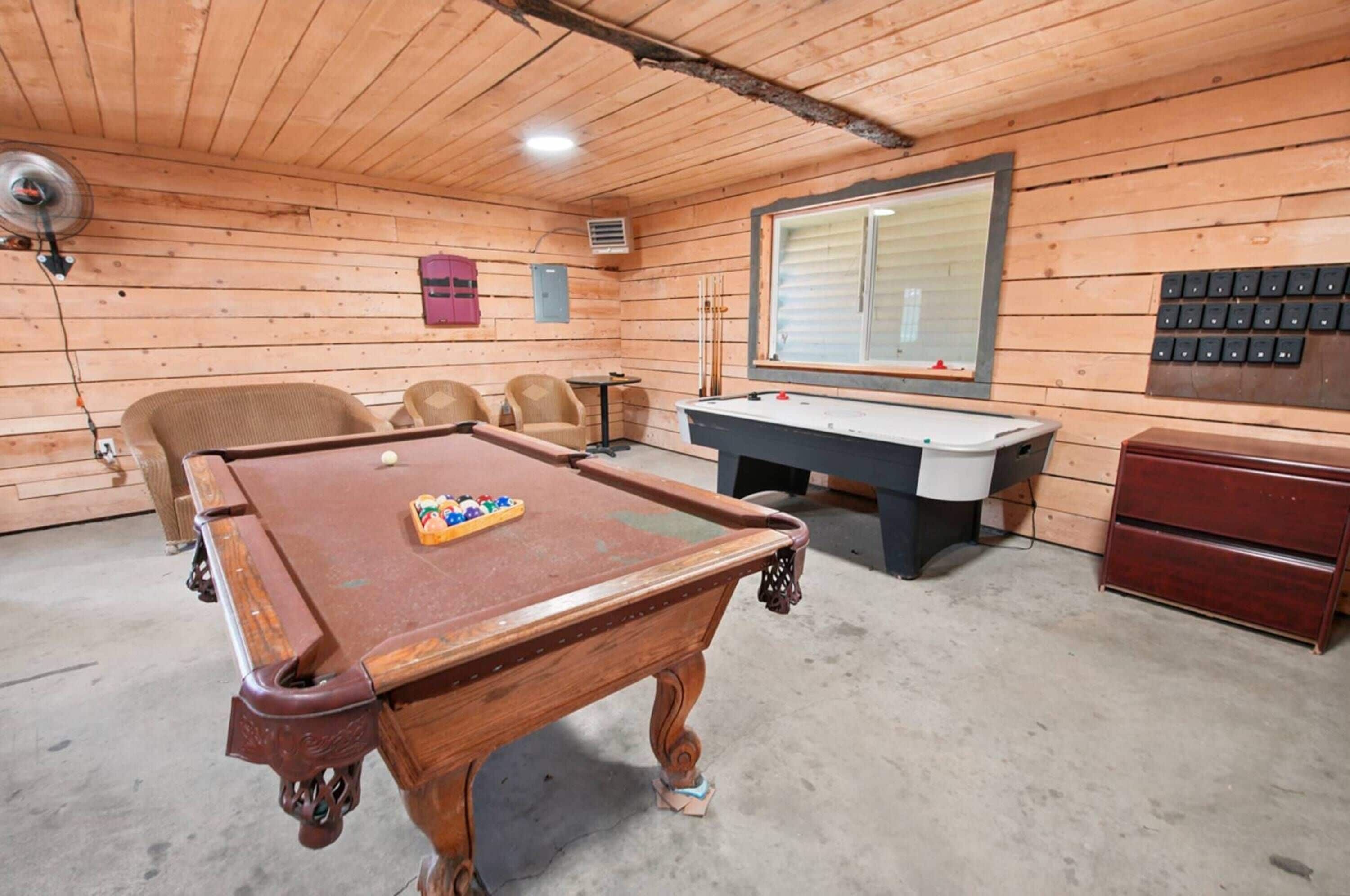 Una habitación de madera con mesa de billar, sillas, escritorio y ventana.