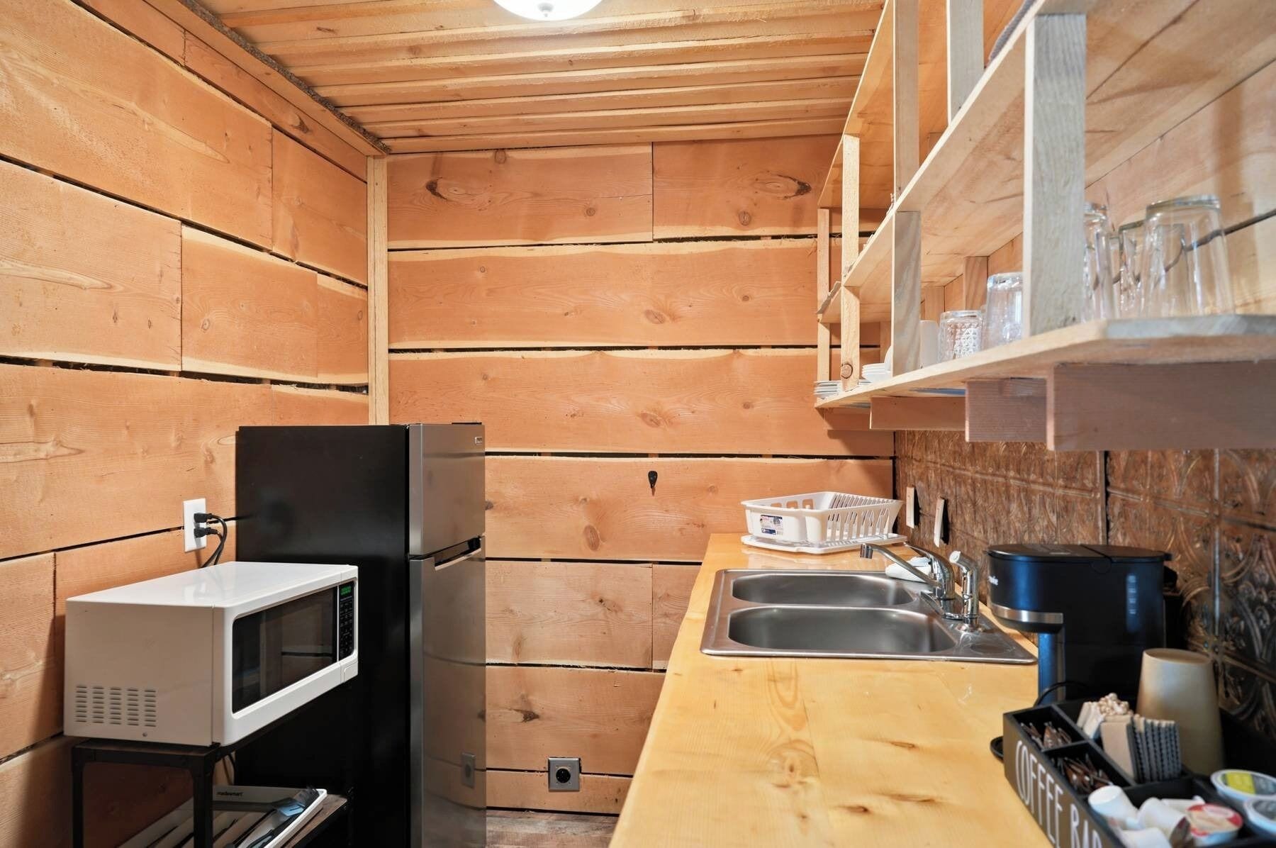 A compact kitchen with wooden walls, a microwave, a sink, and a coffee station.