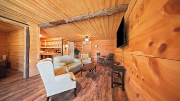 A log cabin interior with a dining area, sofa, TV, and wooden walls.