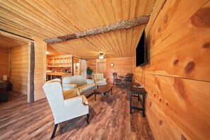 A log cabin interior with a dining area, sofa, TV, and wooden walls. - Birch Glen Hotel (Cascade)