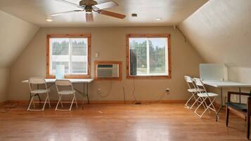 A room with a ceiling fan, two windows with blinds, a desk with a chair, and an air conditioning unit.