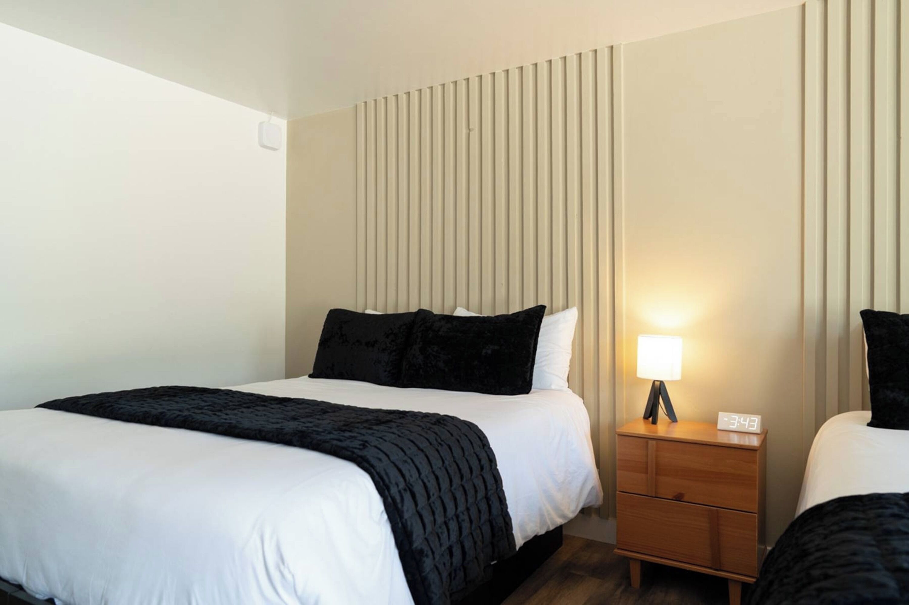 A hotel room with a bed, a nightstand with a lamp, and a wall with vertical blinds.
