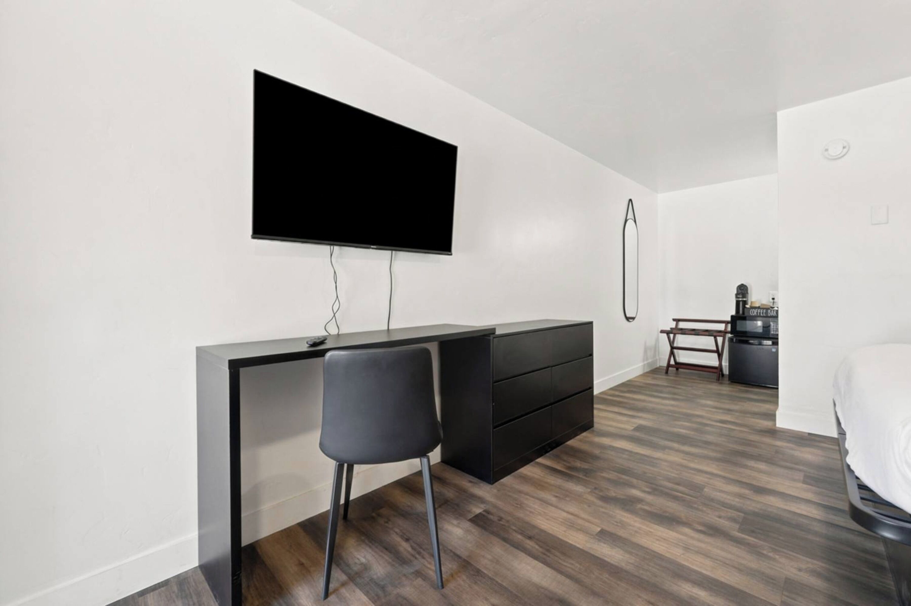 Une chambre moderne comprenant un lit, un bureau avec une chaise, un téléviseur fixé au mur et une machine à café.