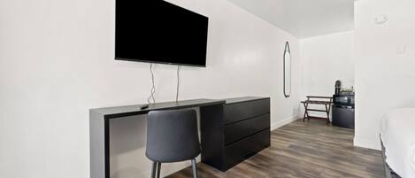 Un dormitorio moderno con cama, escritorio con silla, televisor montado en la pared y cafetera.