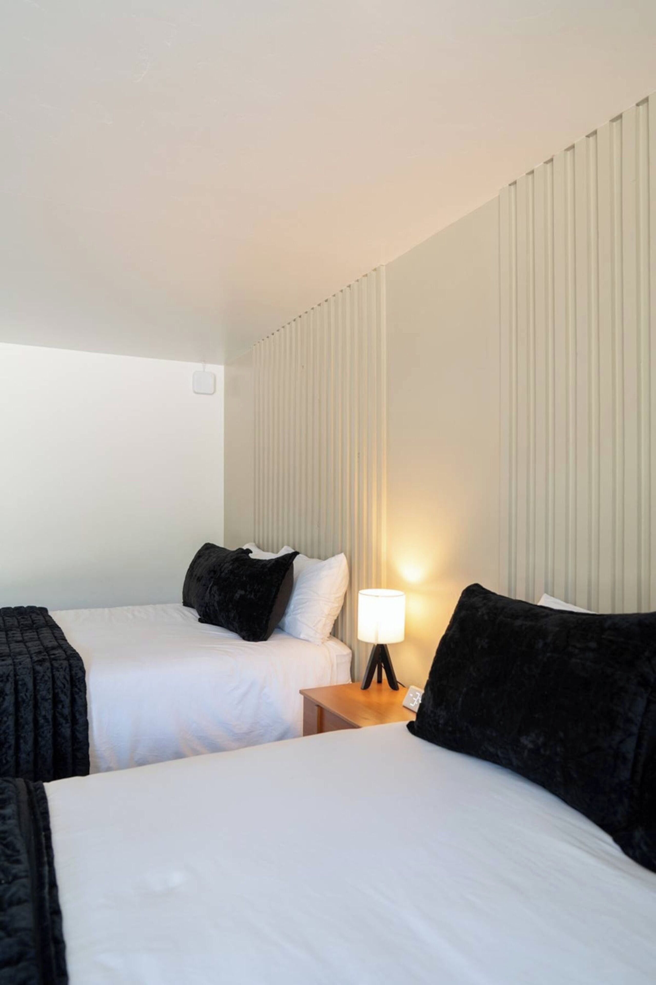 Une chambre d’hôtel avec deux lits, une table de chevet avec une lampe et un luminaire fixé au mur.
