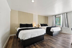 A modern hotel room with two beds, a large window with curtains, and a wooden floor.