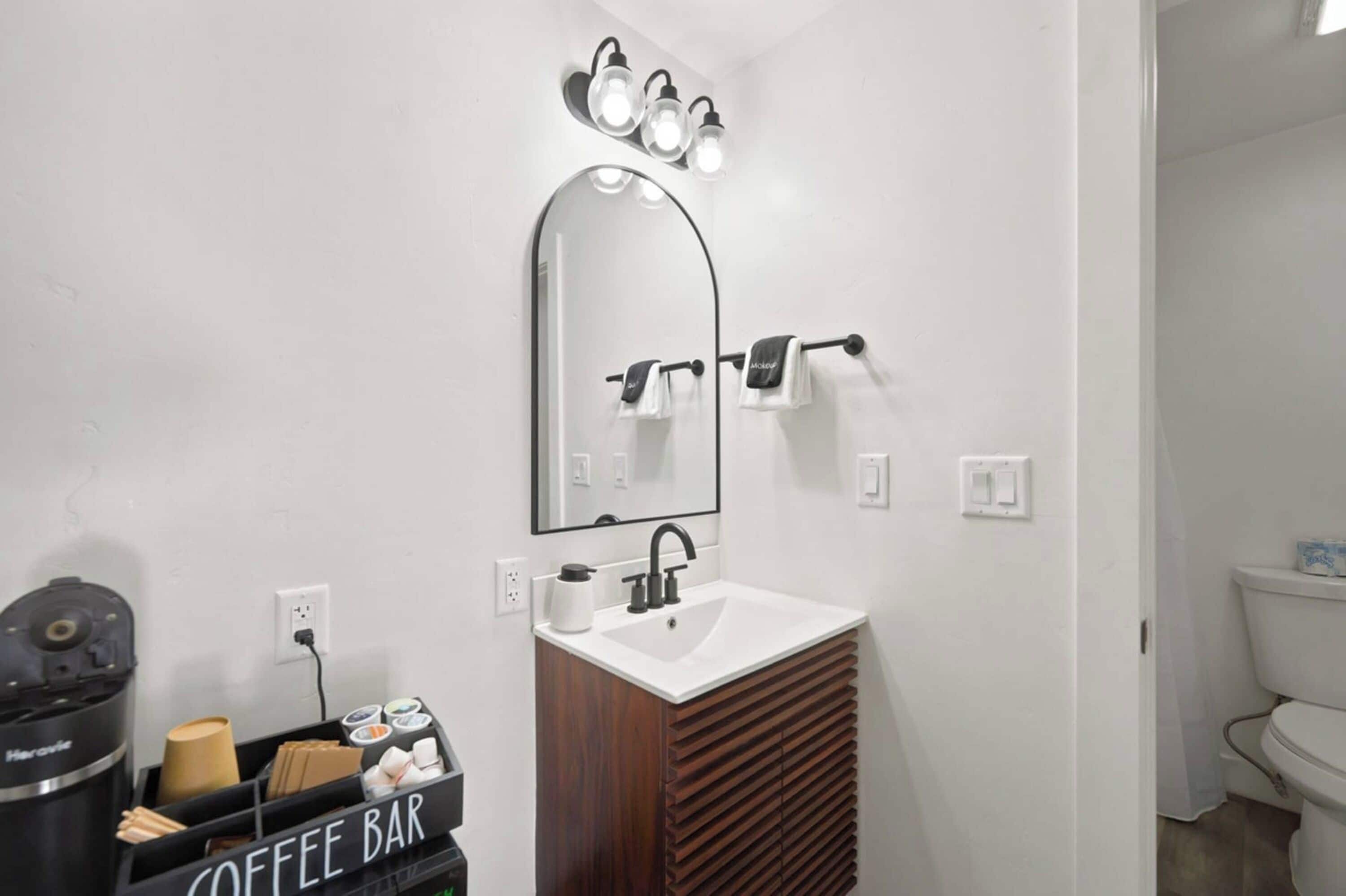 A bathroom with a white sink, a mirror, and a coffee bar.