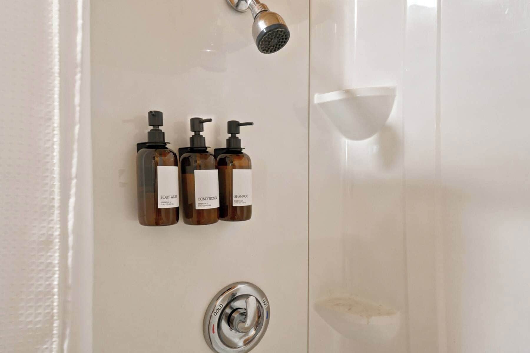 Une salle de bain équipée d’une douche, d’un s èche-mains et de trois flacons de produits de toilette.