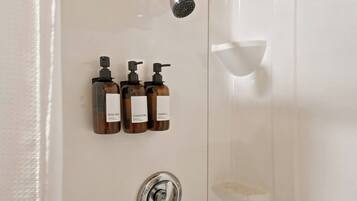 A bathroom with a shower, a hand dryer, and three bottles of toiletries.