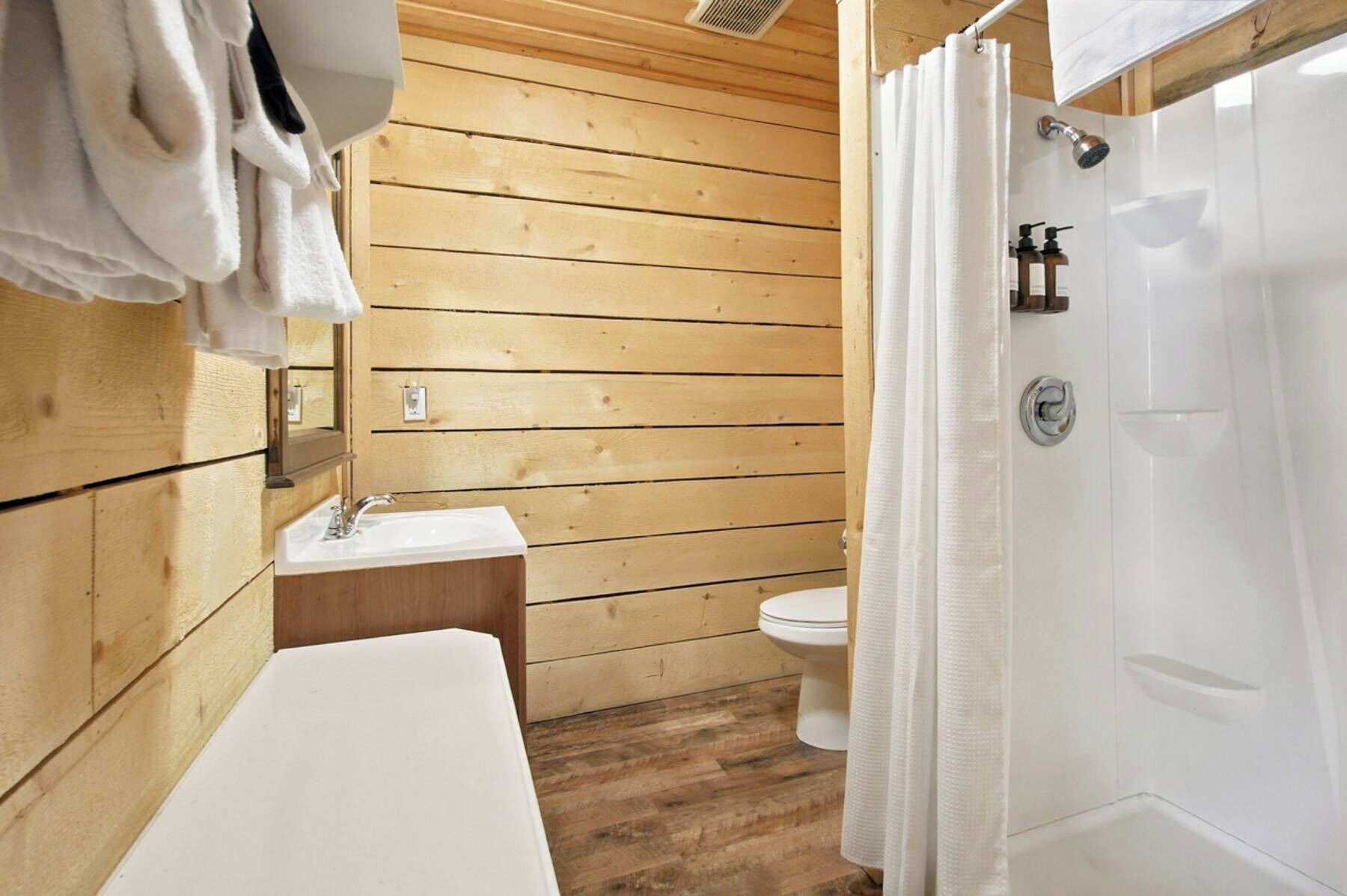 Un baño con paneles de madera, un lavamanos blanco, inodoro y zona de ducha.