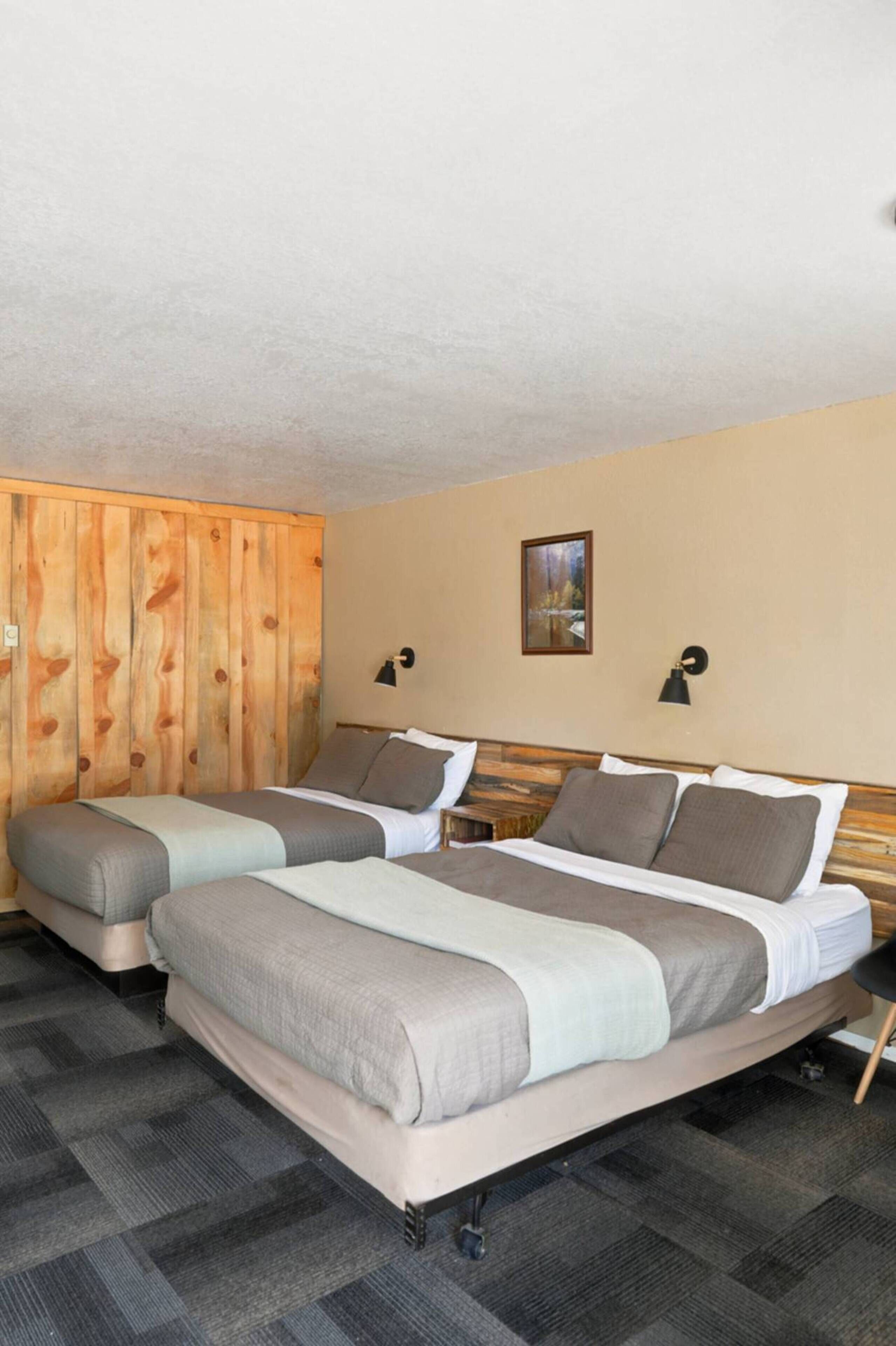 A hotel room with two beds, wooden paneling on one wall, a framed picture on the wall, and a small table.