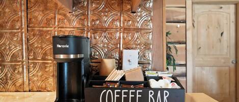 Una cafetera, un letrero que dice 'Coffee Bar' y un mueble de madera con un panel trasero decorativo.