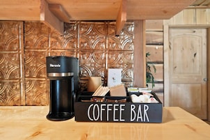 Una cafetera, un letrero que dice 'Coffee Bar' y un mueble de madera con un panel trasero decorativo.