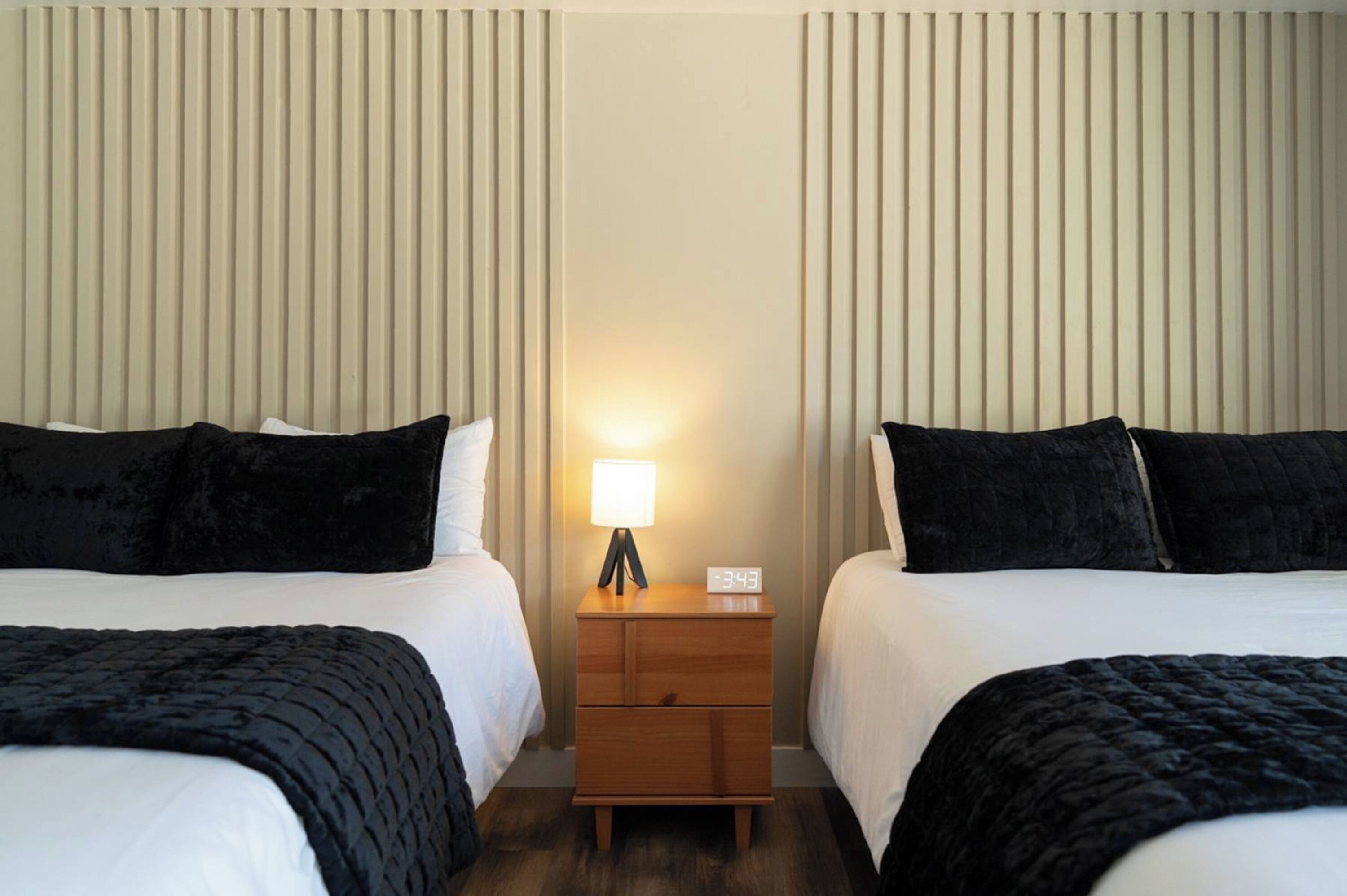 Une chambre d’hôtel avec deux lits, une table de chevet avec une lampe et une horloge numérique.
