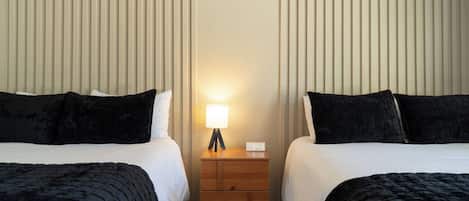 Une chambre d’hôtel avec deux lits, une table de chevet avec une lampe et une horloge numérique.