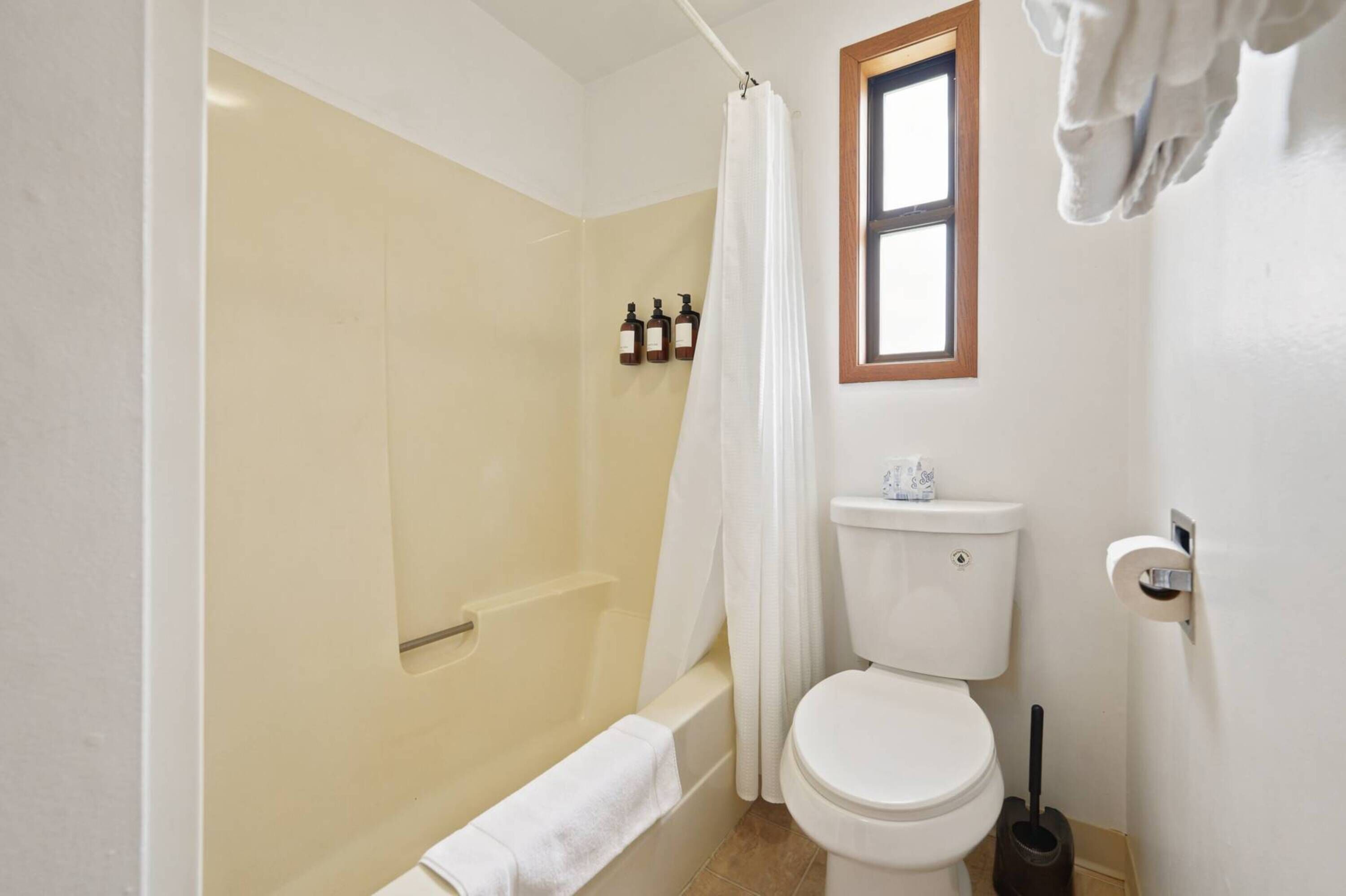 A bathroom with a shower, toilet, and a window.