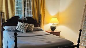 Un lit avec une tête de lit, une table de chevet avec une lampe et une fenêtre avec des rideaux.