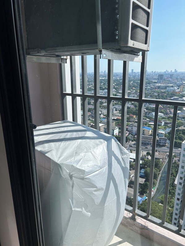 Un balcón con vistas a un paisaje urbano, un objeto blanco en el suelo y una barandilla metálica.