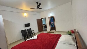 A hotel room with a bed, a desk, two chairs, a television, and a ceiling fan. - Tea Haze Cottage Munnar (Anachal)