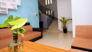A living room with a sofa, a coffee table with a plant, a staircase, and a wall-mounted shelf. - Tea Haze Cottage Munnar (Anachal)