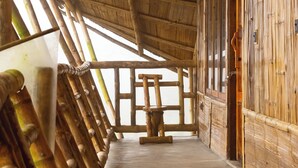 A wooden interior with a thatched roof, a wooden bench, and a view of the outside. - KaatiKaadu (Sakleshpur)