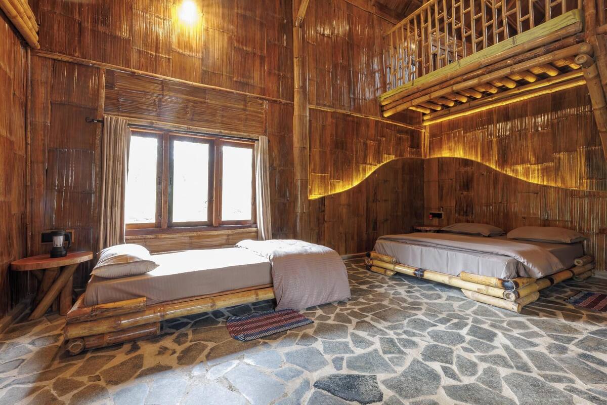 A rustic room with two beds, a stone floor, and wooden walls.