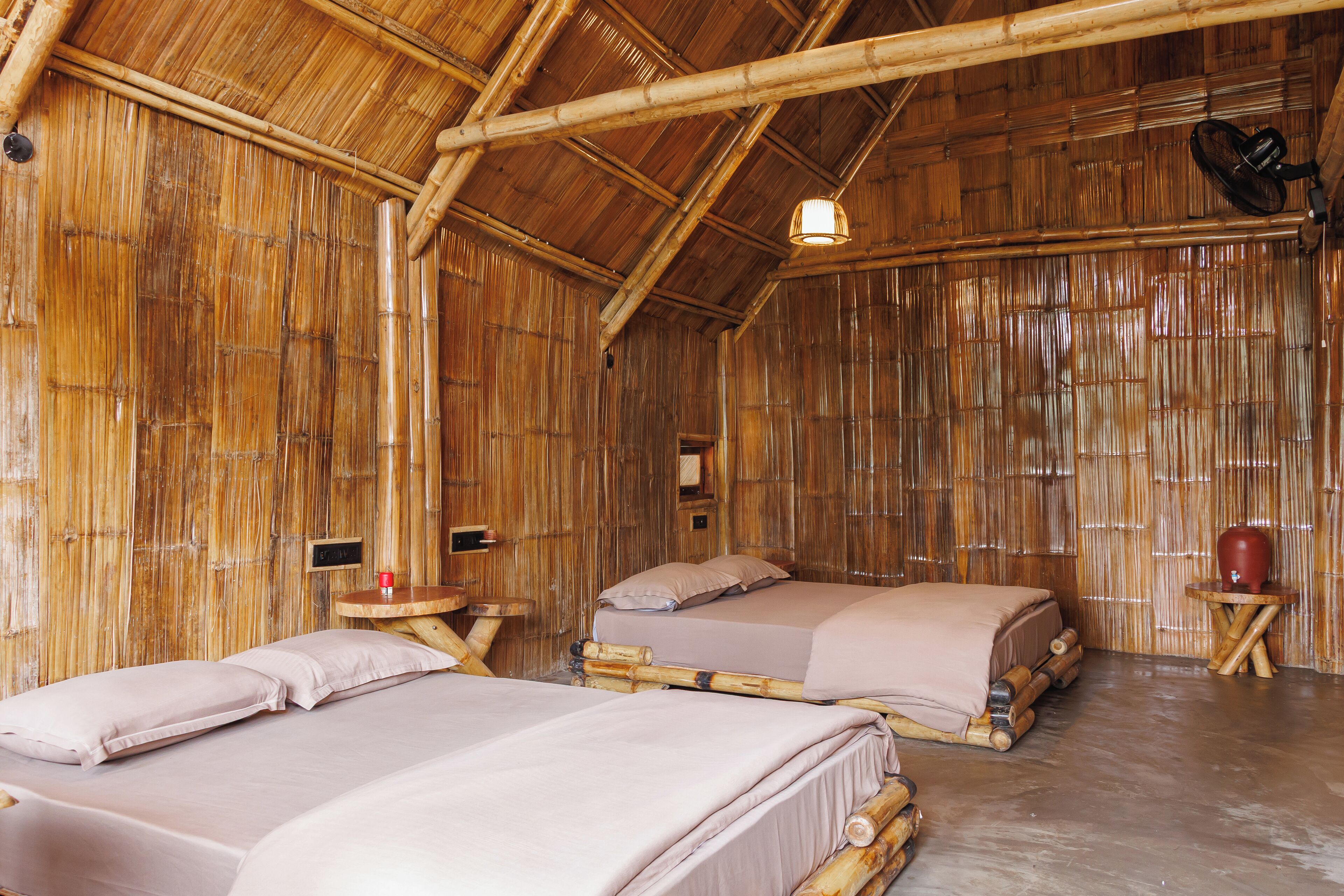 Quarto com tema de bambu, com duas camas, uma mesinha e um candeeiro pendente.