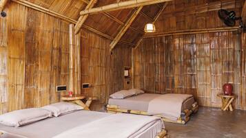 Quarto com tema de bambu, com duas camas, uma mesinha e um candeeiro pendente.