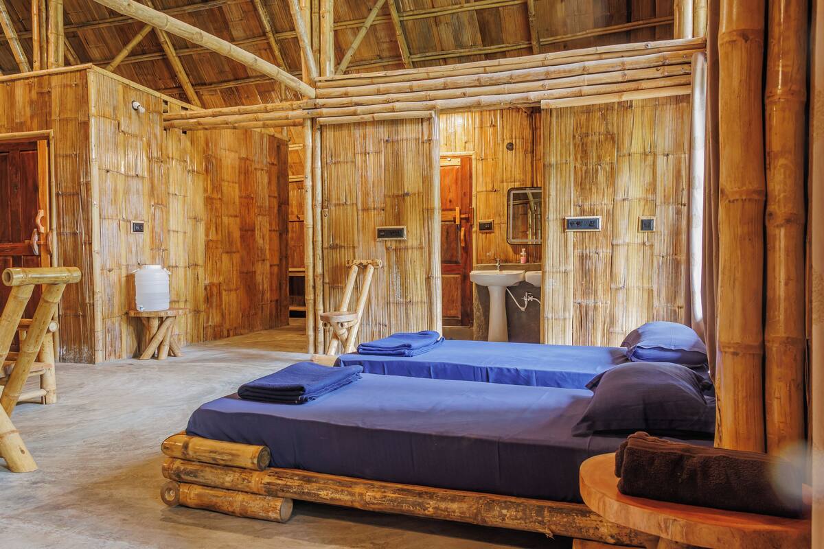 A bamboo-themed room with two beds, a wooden ladder, a sink, and a mirror.