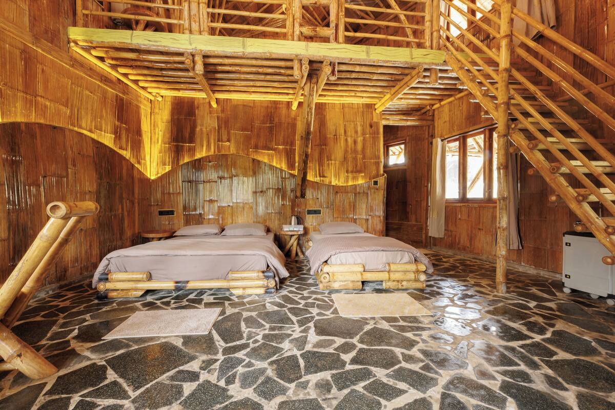 A room with two beds, a stone floor, and a bamboo ceiling.
