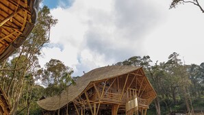 A large, open wooden structure with a curved roof, surrounded by trees. - KaatiKaadu (Sakleshpur)