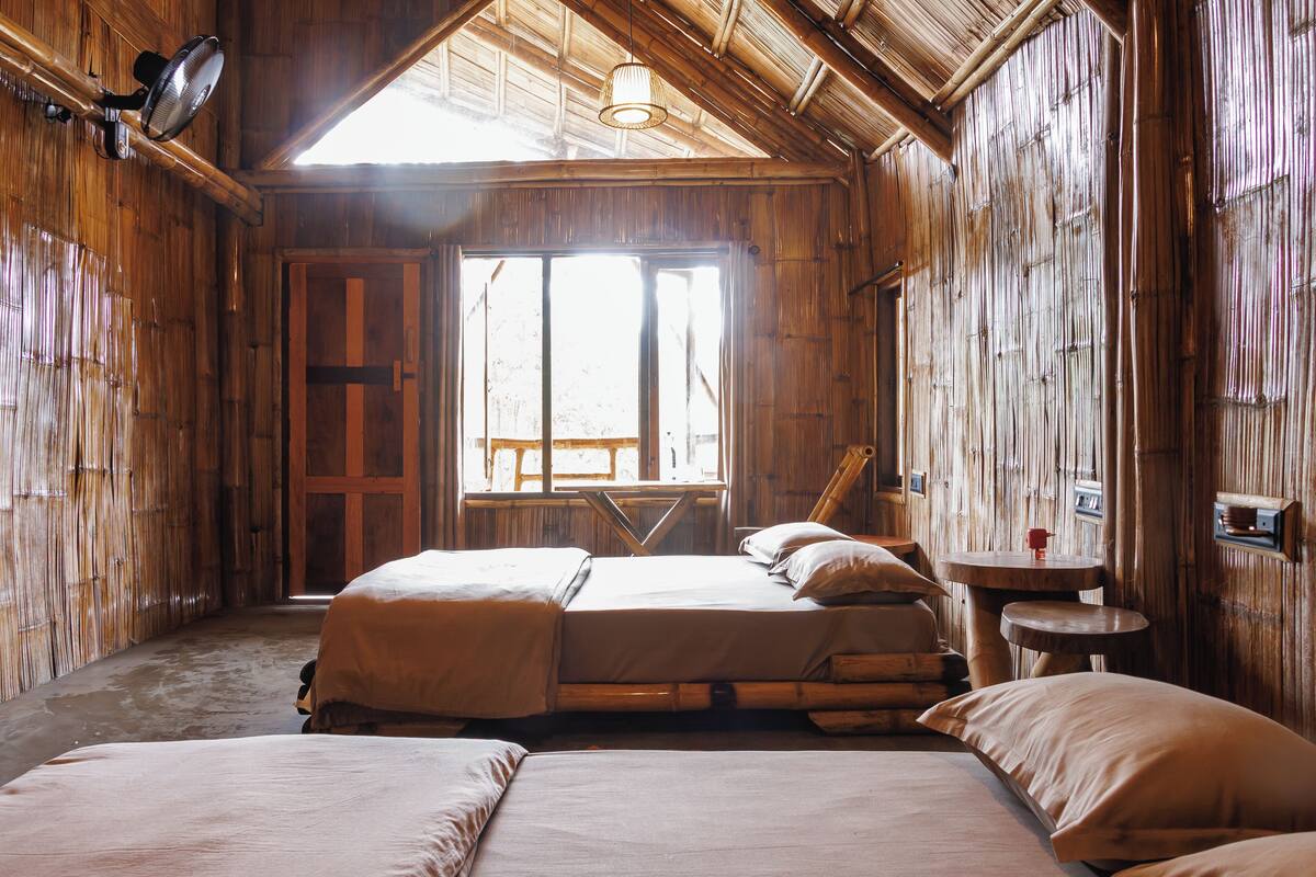 A rustic wooden room with two beds, a small table, and a window with a view.