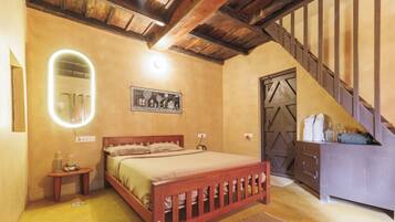 A bedroom with a wooden bed, a bedside table with a lamp, a wall-mounted mirror, and a staircase leading to another room.
