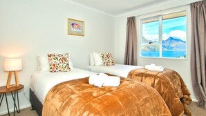 A hotel room with two beds, a window with a mountain view, a lamp, and a framed picture on the wall.