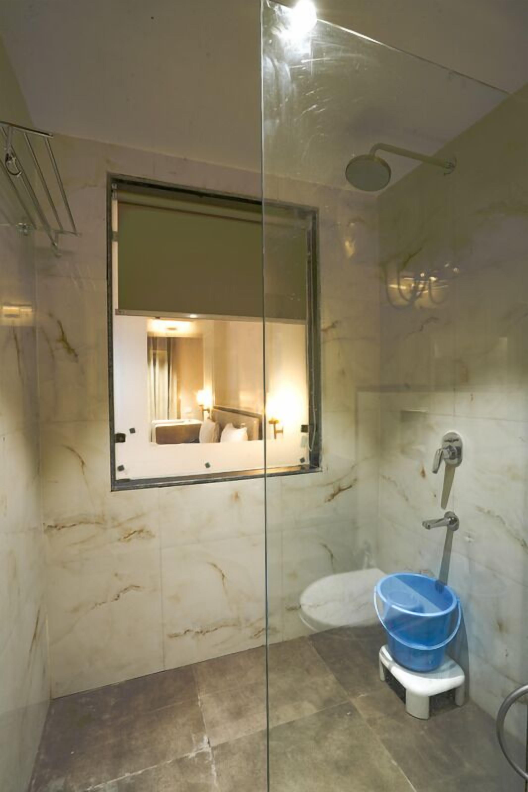 A bathroom with a glass partition, a toilet, a blue basin, and a shower.