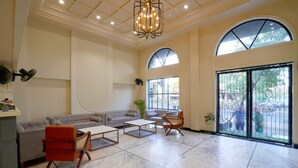 A spacious living area with a large sectional sofa, a coffee table, and a red chair. There is a large arched window and a sliding glass door leading to an outdoor area. - Hotel Square 36 (Kota)