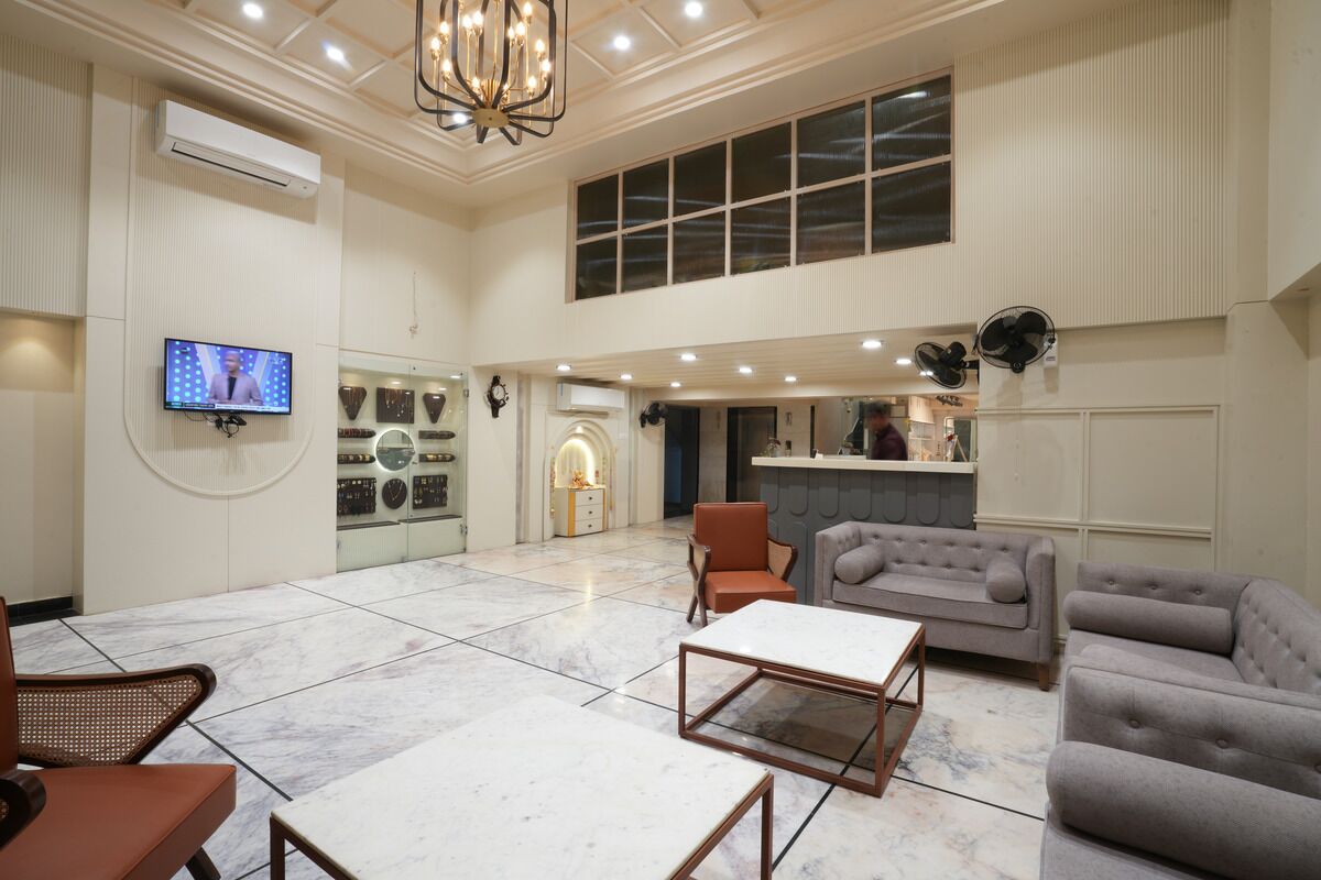 A spacious lobby with a marble floor, a television mounted on the wall, a reception desk, and a seating area with sofas and chairs.