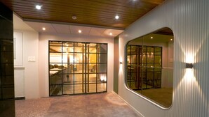 A modern interior with a wooden ceiling, a large glass door leading to a dining area, and a curved wall with a mirror. - Hotel Square 36 (Kota)