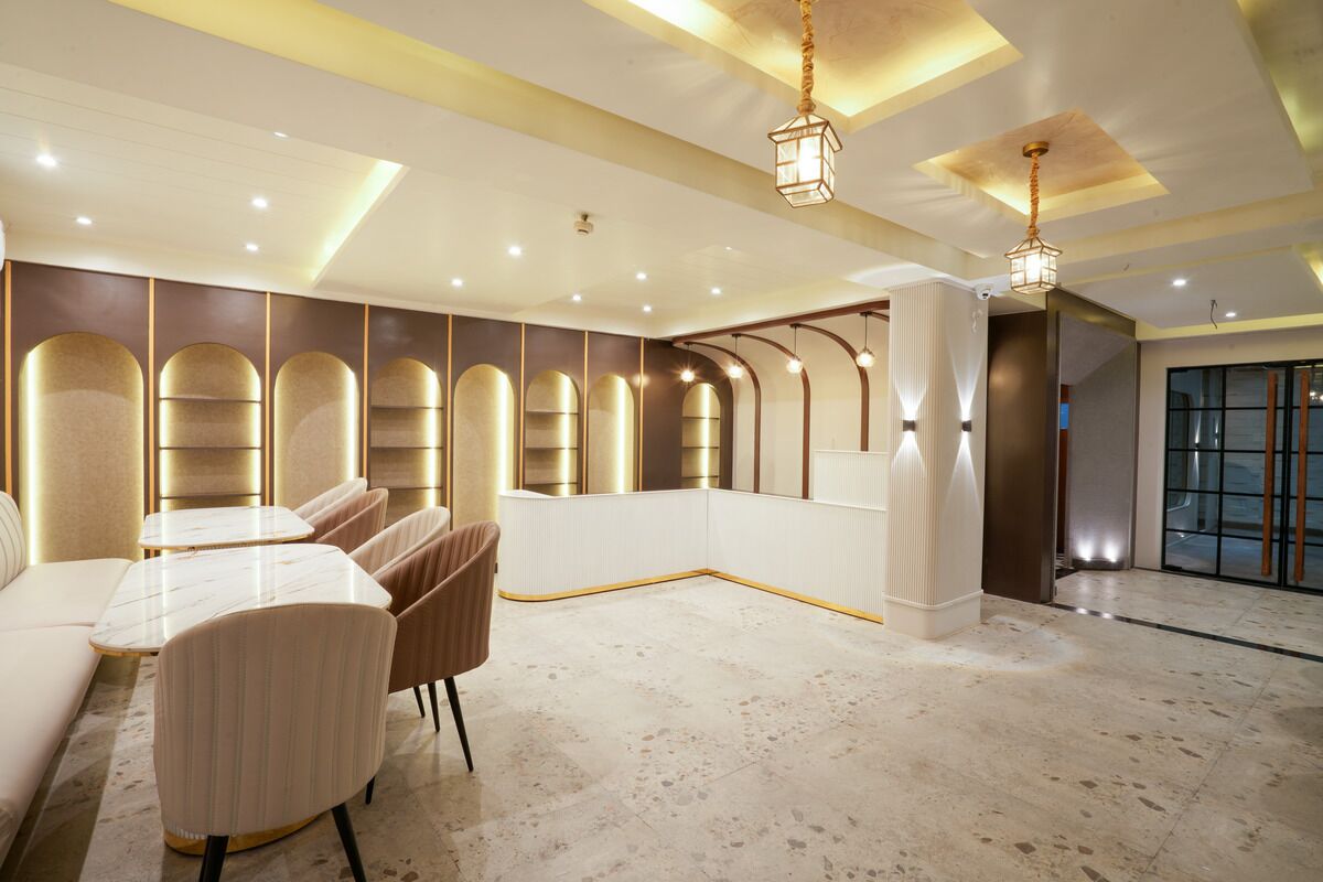 A modern hotel lobby with a marble floor, seating area with tables and chairs, and a large glass door entrance.